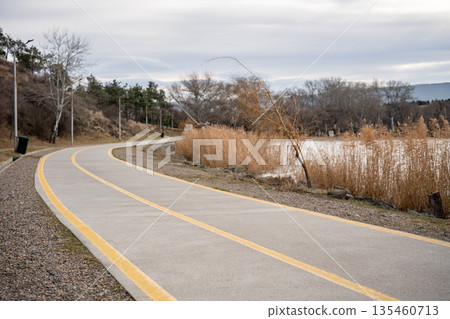 Walking road around lake on winter day, pathway for active sports, cycling and running near pond. Walking road around lake on winter day, pathway for active sports, cycling and running near pond. 135460713