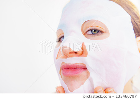 Woman applying sheet mask on face Woman applying sheet mask on face 135460797