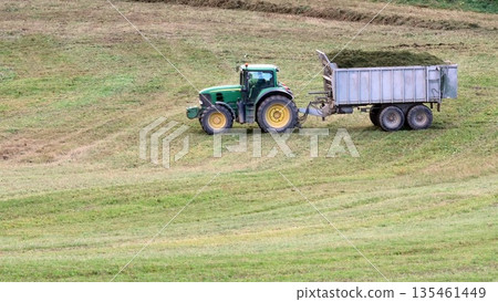 A tractor with a loaded trailer passes through a green field 135461449