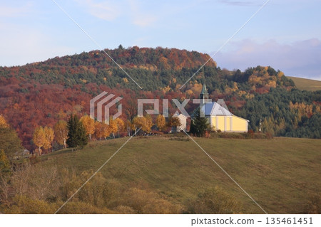 The church stands on a hill with a colorful forest in the background The church stands on a hill with a colorful forest in the background 135461451