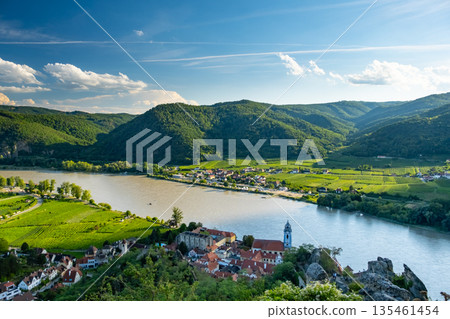 Wachau Valley offers a stunning panorama of the Danube River in Ausrtia. The quaint village of Durnstein is seen with its vineyards and historical architecture along the riverbank. Wachau Valley offers a stunning panorama of the Danube River in Ausrtia. The quaint village of Durnstein is seen with its vineyards and historical architecture along the riverbank. 135461454