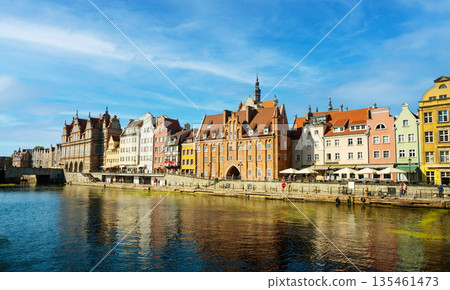 Charming historic architecture lines the waterfront of Gdansk under a clear blue sky. The river is bustling with boats, offering a vibrant scene with the city's iconic brick buildings 135461473