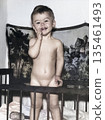 A vintage portrait of a boy standing in his crib. The child is smiling. Retro photo from 1969. 135461493