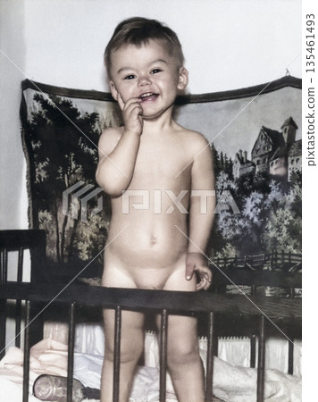 A vintage portrait of a boy standing in his crib. The child is smiling. Retro photo from 1969. 135461493