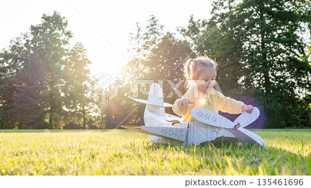 Cardboard airplane. Child pilot play outdoor. Toddler costume girl field yellow. Cardboard airplane. Child pilot play outdoor. Toddler costume girl field yellow. 135461696