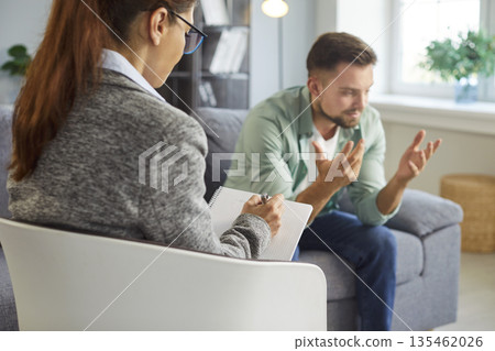 Male patient speaking with psychologist in therapy session in modern office 135462026
