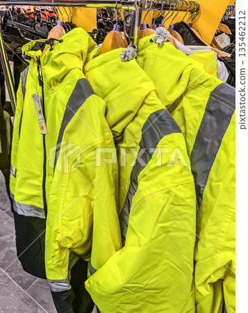 A rack of bright yellow high-visibility safety jackets with reflective stripes hanging in a store. Essential protective outerwear for workers.. High quality photo A rack of bright yellow high-visibility safety jackets with reflective stripes hanging in a store. Essential protective outerwear for workers.. High quality photo 135462212