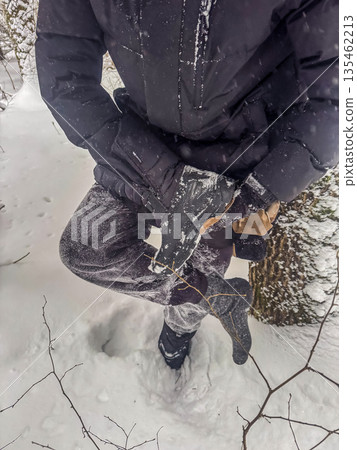 A first-person view of a hiker adjusting a snow-covered boot while standing in deep snow in a winter forest, preparing for an outdoor adventure. High quality photo A first-person view of a hiker adjusting a snow-covered boot while standing in deep snow in a winter forest, preparing for an outdoor adventure. High quality photo 135462213