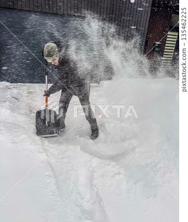 An action shot of a person clearing a path, throwing a large spray of powdery snow with a shovel during a fierce winter blizzard.. High quality photo 135462225