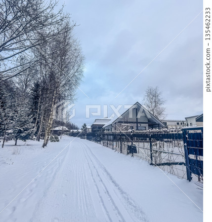 A fresh set of cross-country ski tracks runs down a snow-covered road past modern houses in a quiet, peaceful winter village scene. High quality photo A fresh set of cross-country ski tracks runs down a snow-covered road past modern houses in a quiet, peaceful winter village scene. High quality photo 135462233