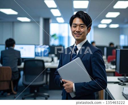 辦公室裡，一位商務人士站在電腦前。 135463222