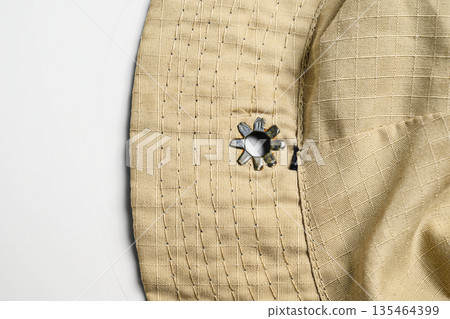 Macro shot of a tan boonie hat's brim and crown, featuring durable ripstop fabric, parallel stitching, and a star-shaped metal ventilation eyelet on a white background Macro shot of a tan boonie hat's brim and crown, featuring durable ripstop fabric, parallel stitching, and a star-shaped metal ventilation eyelet on a white background 135464399