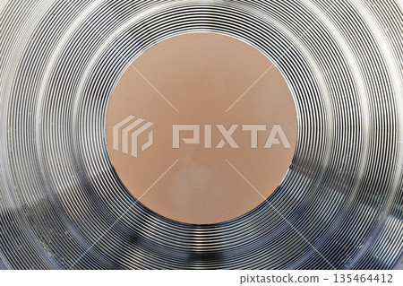 Macro shot of the bottom of a professional cookware pan showing metallic concentric ridges for even heat distribution and a central orange core. Industrial and abstract background Macro shot of the bottom of a professional cookware pan showing metallic concentric ridges for even heat distribution and a central orange core. Industrial and abstract background 135464412