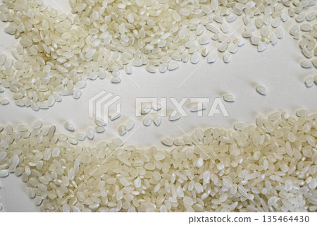 Close-up of high-quality raw white rice grains spread on a white surface with a central empty space for text. Perfect for food, cooking, and health-related designs 135464430