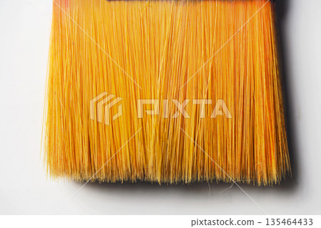 Macro view of a flat paintbrush with vibrant orange synthetic bristles and a metal ferrule. Isolated on a white background, perfect for art, craft, and renovation concepts 135464433