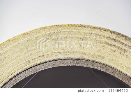 A detailed macro shot showing the side profile and layered texture of a roll of paper masking tape on a cardboard core, highlighting its industrial and craft use A detailed macro shot showing the side profile and layered texture of a roll of paper masking tape on a cardboard core, highlighting its industrial and craft use 135464453
