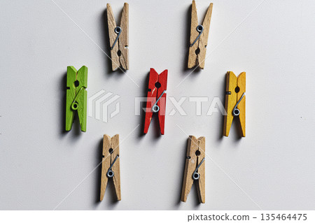 Top view of a group of seven wooden clothespins in green, red, yellow and natural colors on a white textured background, illustrating leadership and individuality concepts Top view of a group of seven wooden clothespins in green, red, yellow and natural colors on a white textured background, illustrating leadership and individuality concepts 135464475