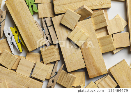 Top-down view of scattered wooden blocks in various sizes and shapes mixed with small colorful and natural wood clothespins. Ideal for craft, hobby, and DIY project concepts 135464479