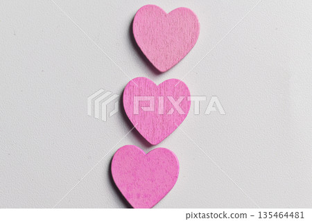 A vertical arrangement of three small, bright pink wooden heart shapes centered on a textured white surface, perfect for Valentine's Day or romantic themes A vertical arrangement of three small, bright pink wooden heart shapes centered on a textured white surface, perfect for Valentine's Day or romantic themes 135464481