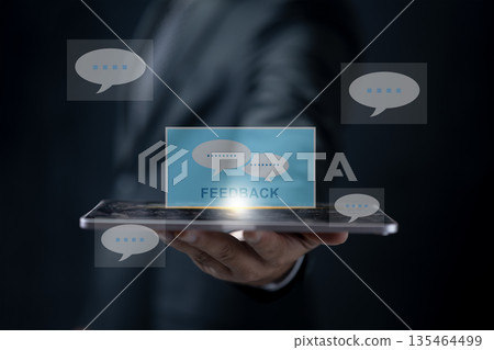 Businessman holding a tablet with a glowing feedback hologram and speech bubble icons. Concept for customer reviews, online satisfaction surveys, and digital business communication Businessman holding a tablet with a glowing feedback hologram and speech bubble icons. Concept for customer reviews, online satisfaction surveys, and digital business communication 135464499