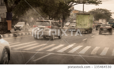 Busy urban traffic with cars and a truck driving through thick air pollution and smog on a city road. Represents environmental issues, climate change, and health risks in cities Busy urban traffic with cars and a truck driving through thick air pollution and smog on a city road. Represents environmental issues, climate change, and health risks in cities 135464530