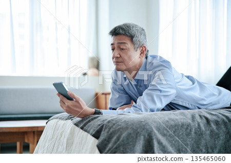 一位老年男子躺在床上,看著他的智慧型手機。 一位老年男子躺在床上,看著他的智慧型手機。 135465060