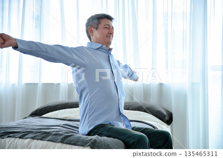 一位老人坐在床上伸懶腰。 135465311