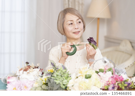 Senior woman arranging flowers as a hobby in the living room 135466891