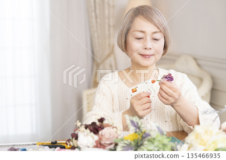 Senior woman arranging flowers as a hobby in the living room 135466935