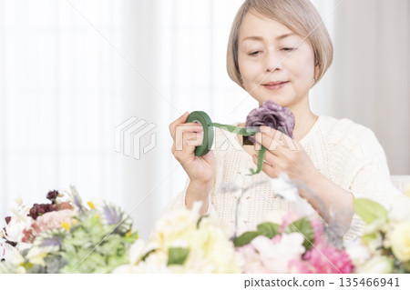 Senior woman arranging flowers as a hobby in the living room 135466941