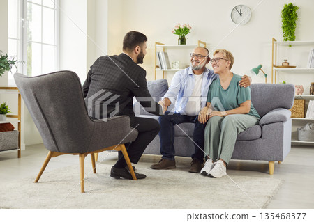 Senior couple shaking hands with real estate agent after signing agreement at home Senior couple shaking hands with real estate agent after signing agreement at home 135468377