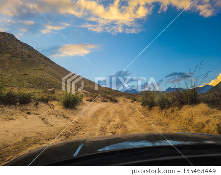 View on dirt road in mountainous landscape at twilight from car driver perspective View on dirt road in mountainous landscape at twilight from car driver perspective 135468449