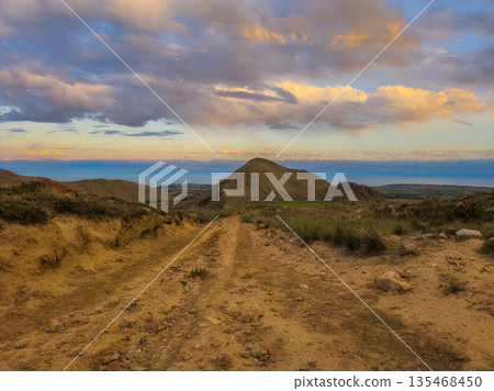 Dirt road leading through hilly landscape towards distant Issyk-Kul lake water Dirt road leading through hilly landscape towards distant Issyk-Kul lake water 135468450