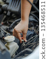 Close up of a  hand of woman pulling an engine oil dipstick to inspect oil level 135468511