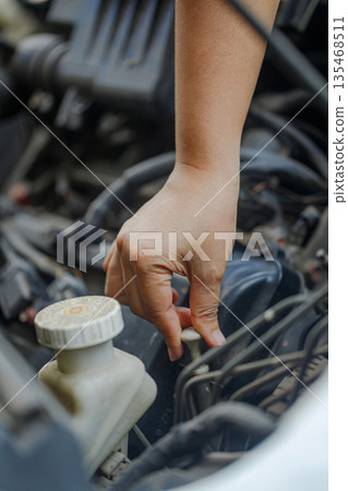 Close up of a  hand of woman pulling an engine oil dipstick to inspect oil level 135468511