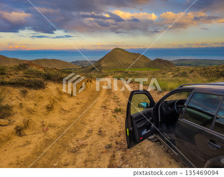 Car with open door stopped on dirt road at sunset in rural landscape Car with open door stopped on dirt road at sunset in rural landscape 135469094