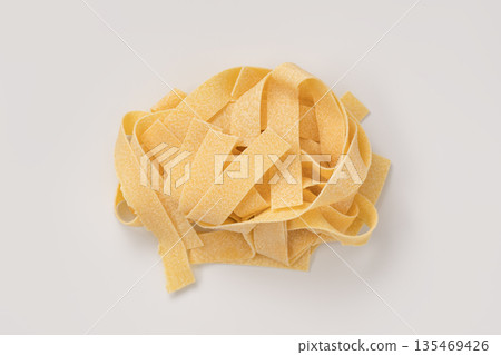 Italian dry fettuccine or tagliatelle pasta over white background with shadow top view 135469426