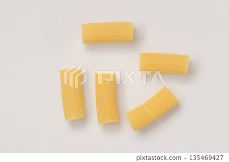 Italian dry rigatoni pasta over white background with shadow top view 135469427