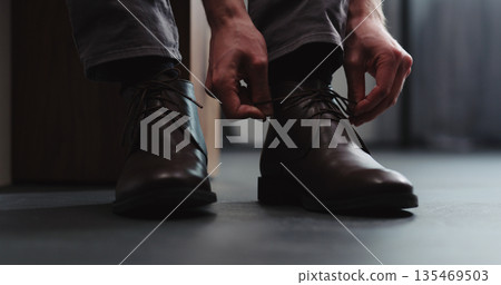 Young man put on his brown leather chukka boots indoor Young man put on his brown leather chukka boots indoor 135469503