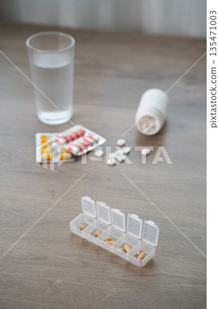 Flat lay of medicines with water glass and pill organizer on table, daily medication schedule, healthcare treatment, dosage planning, copy space background. Flat lay of medicines with water glass and pill organizer on table, daily medication schedule, healthcare treatment, dosage planning, copy space background. 135471003