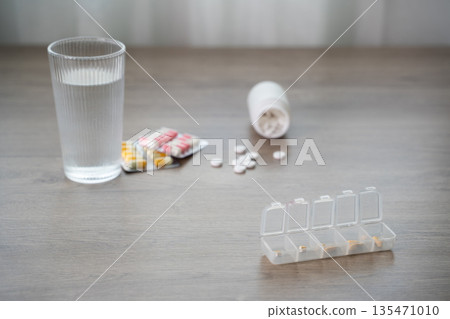 Pill organizer with daily on a table with a glass of water, blister packs, copy space for medication schedule, healthcare, and adherence flatlay, dosage, routine 135471010