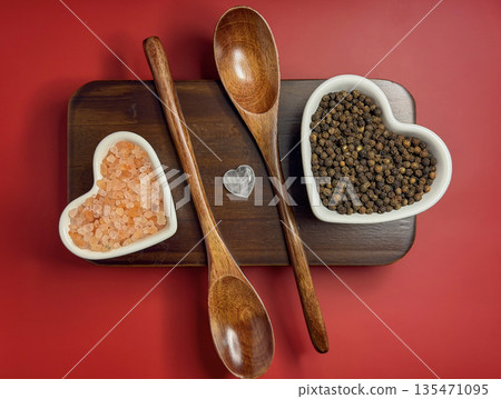 Heart Shaped Bowls of Pink Salt and Black Pepper with Wooden Spoons on Red Background Heart Shaped Bowls of Pink Salt and Black Pepper with Wooden Spoons on Red Background 135471095