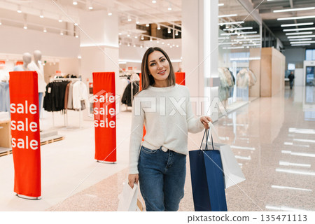 Happy Woman with Shopping Bags Stands Confidently in Store Aisle 135471113