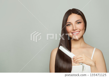Pretty woman brunette with long straight smooth hairstyle using hair straightener iron Pretty woman brunette with long straight smooth hairstyle using hair straightener iron 135471125