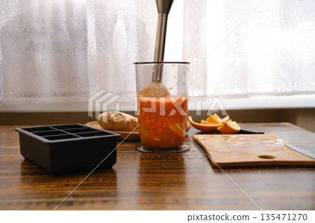 Mixing sea buckthorn and orange in a jar with immersion blender on a wooden table near the window Mixing sea buckthorn and orange in a jar with immersion blender on a wooden table near the window 135471270