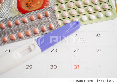 Pregnancy test with birth control pills and condom for female on calendar, ovulation day. 135471509
