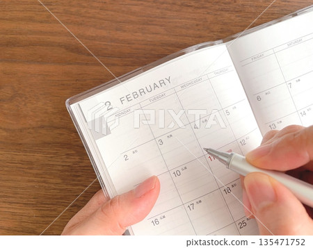 女人的手正在木桌上填寫行程表。 135471752