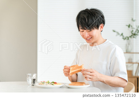 年輕的亞洲男子早餐吃烤麵包和沙拉。 135472110