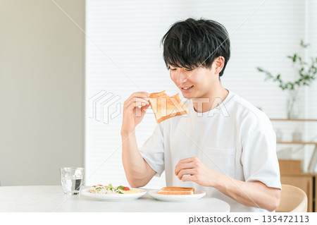 年輕的亞洲男子早餐吃烤麵包和沙拉。 135472113