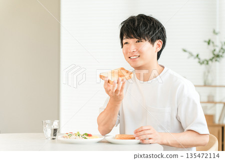 年輕的亞洲男子早餐吃烤麵包和沙拉。 年輕的亞洲男子早餐吃烤麵包和沙拉。 135472114